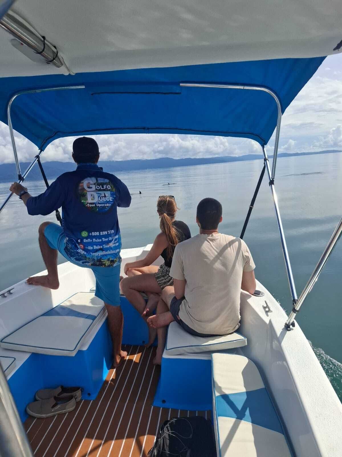 Trois personnes se trouvent dans un bateau équipé d’un auvent, d’une glacière et d’une paire de chaussures posées sur le pont.