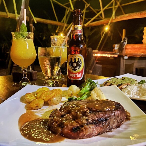 Uma refeição com bife, legumes e uma garrafa de cerveja em cima de uma mesa.
