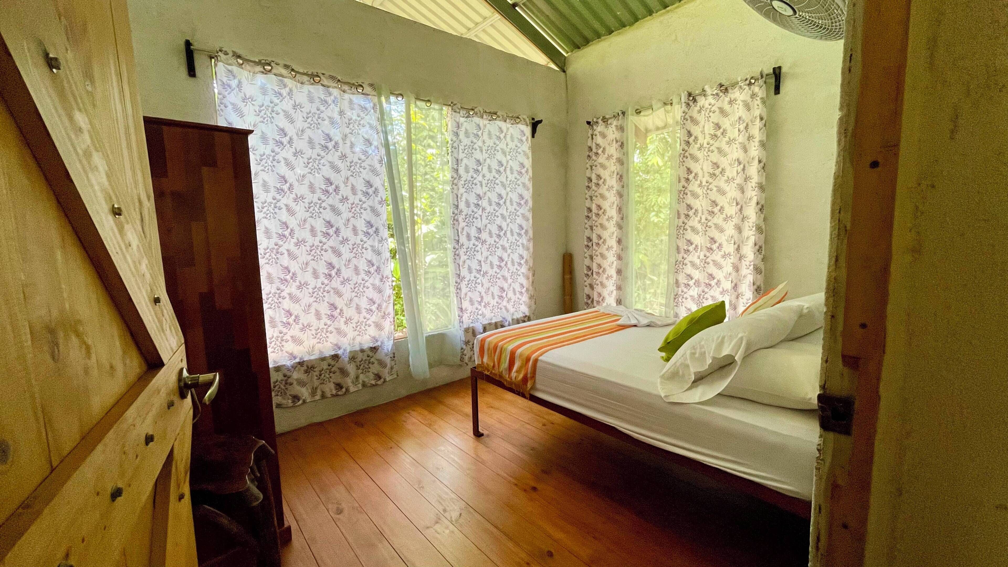 A bedroom with a bed, curtains, a wooden floor, and a window.