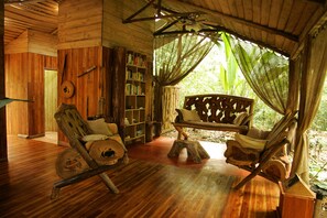 Um interior em madeira com uma rede, estantes de livros e uma cadeira rústica.