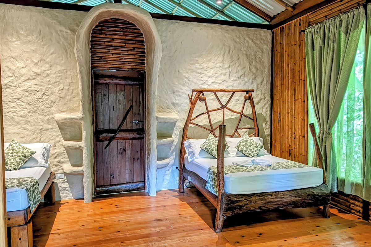 A rustic bedroom with a wooden four-poster bed, a stone archway, and a wooden door.