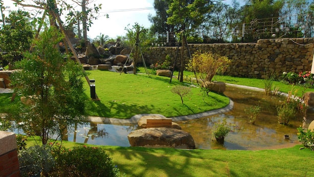 Un jardín bien cuidado con un estanque, muros de piedra y diversas plantas.