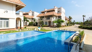 Una piscina con solárium y pavimento de baldosas, rodeada de edificios con un estilo arquitectónico uniforme, que incluyen balcones y un cielo despejado.