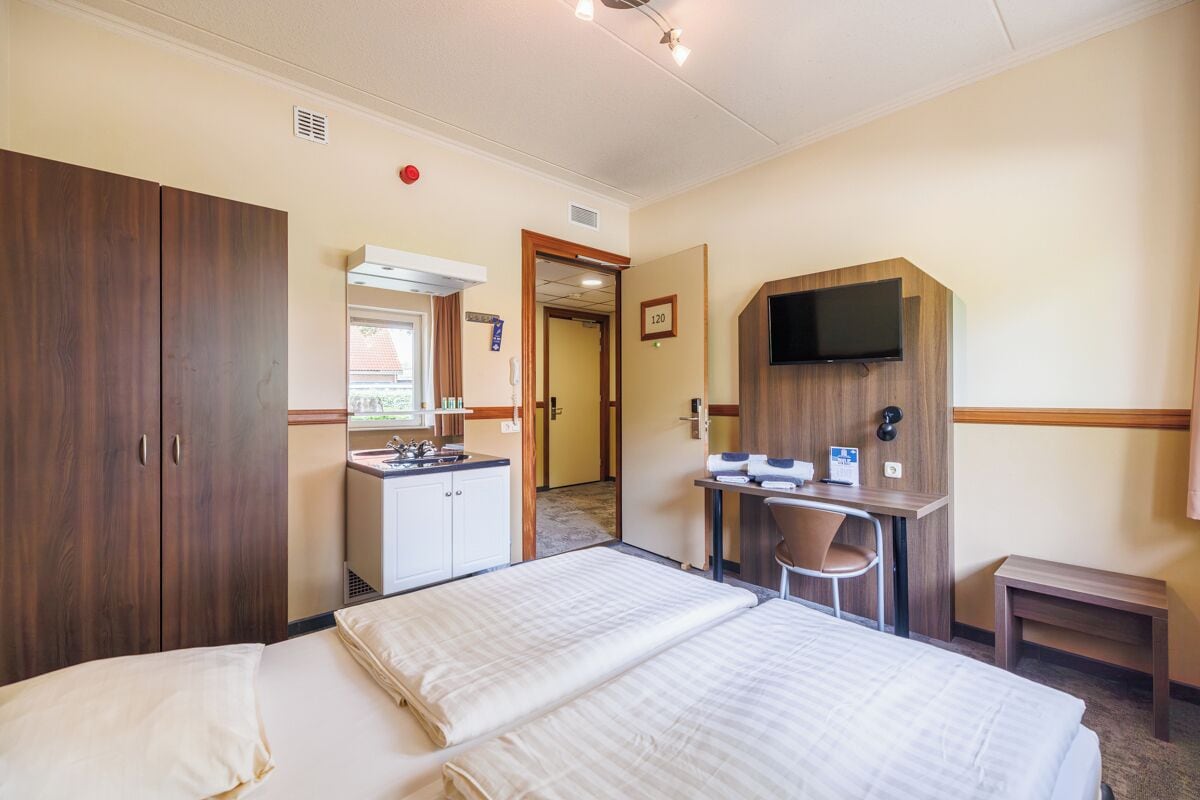 A hotel room with two beds, a desk with a chair, a TV, and a kitchenette.