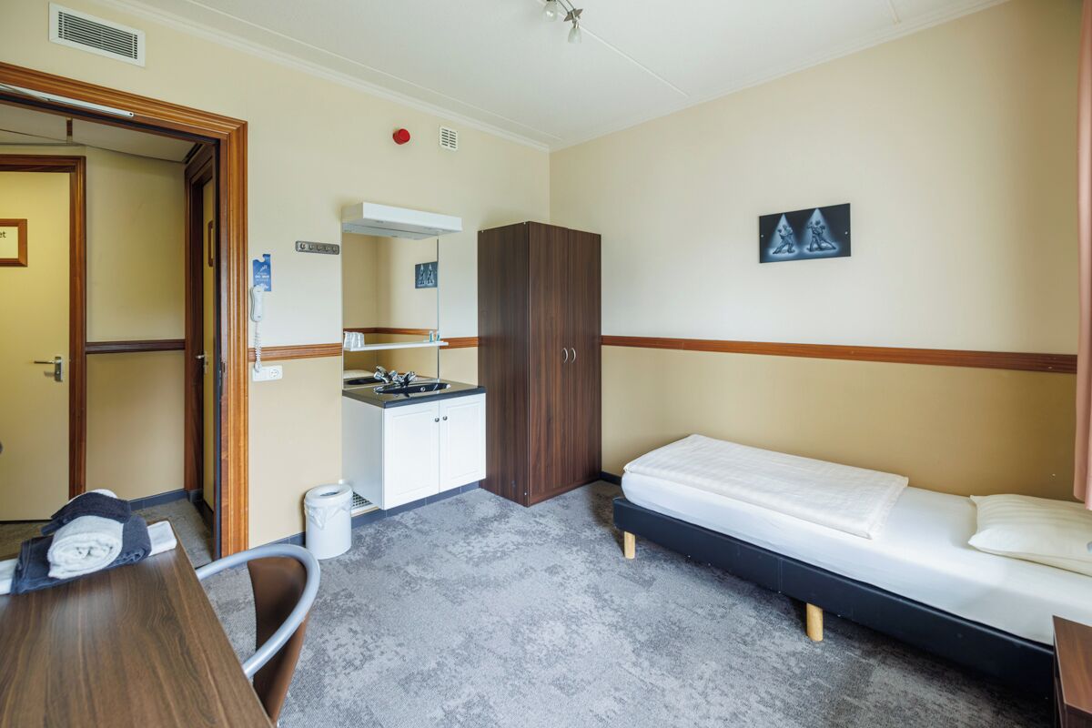 Een compacte hotelkamer met een bed, bureau, kledingkast, een kleine kitchenette en een badkamer.