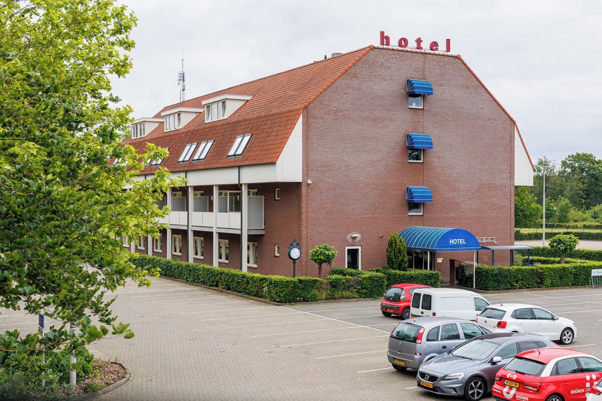A hotel with a red brick facade, a covered entrance, and a parking lot with several cars.