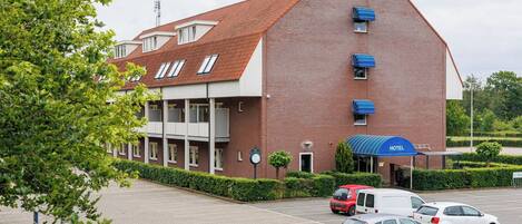 Un hotel con fachada de ladrillo rojo, un acceso cubierto y un estacionamiento con varios coches.