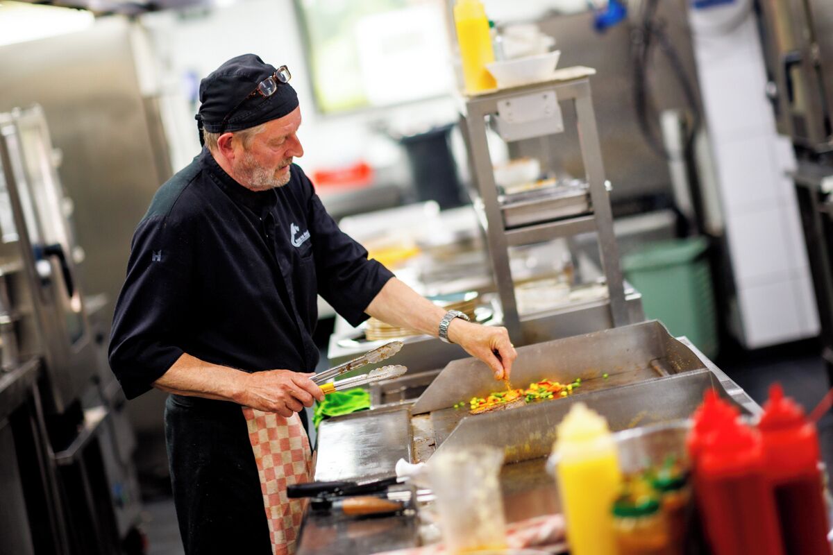 Un chef préparant des plats dans une cuisine professionnelle équipée d’appareils en acier inoxydable et d’une variété de condiments.