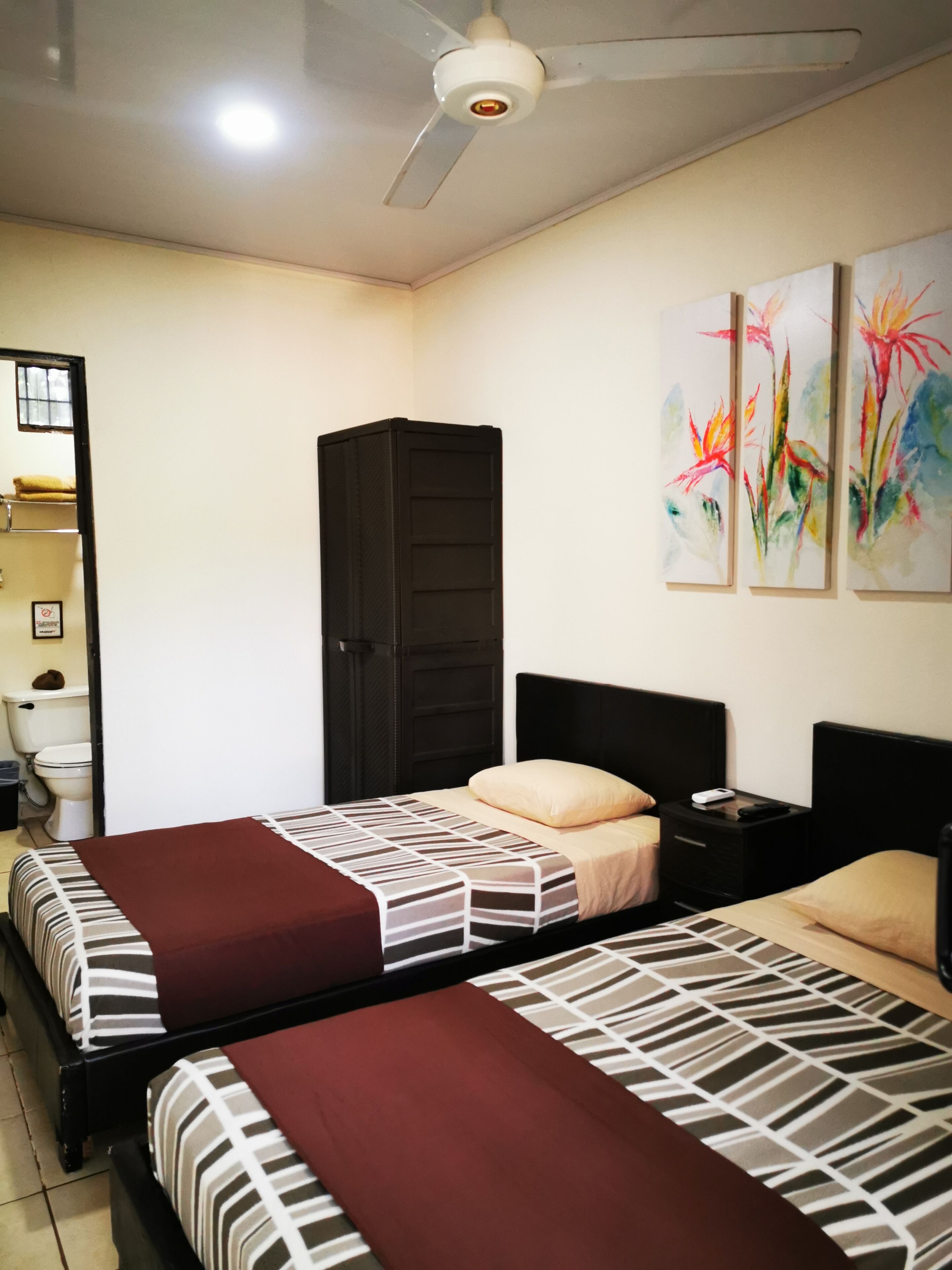 A hotel room with two beds, a wardrobe, a nightstand, and a ceiling fan.
