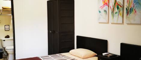 A hotel room with two beds, a wardrobe, a nightstand, and a ceiling fan.