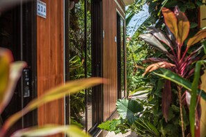 A wooden building with a sliding glass door, surrounded by lush green plants.
