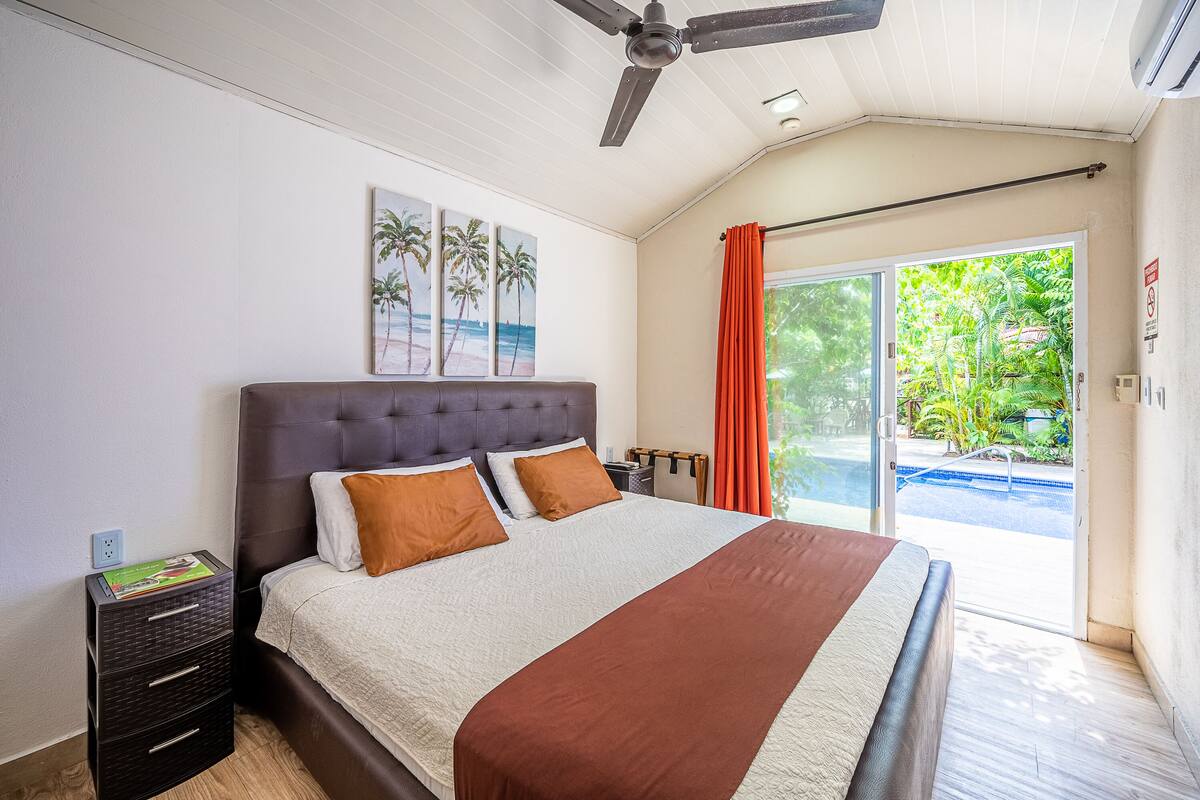A bedroom with a large bed, a ceiling fan, and a view of a swimming pool through a glass door.