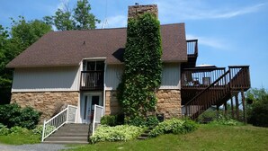 A stone building with a brown roof, a central chimney, and a staircase leading to a balcony.