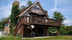 A two-story house with a wooden balcony, a stone chimney, and a satellite dish.