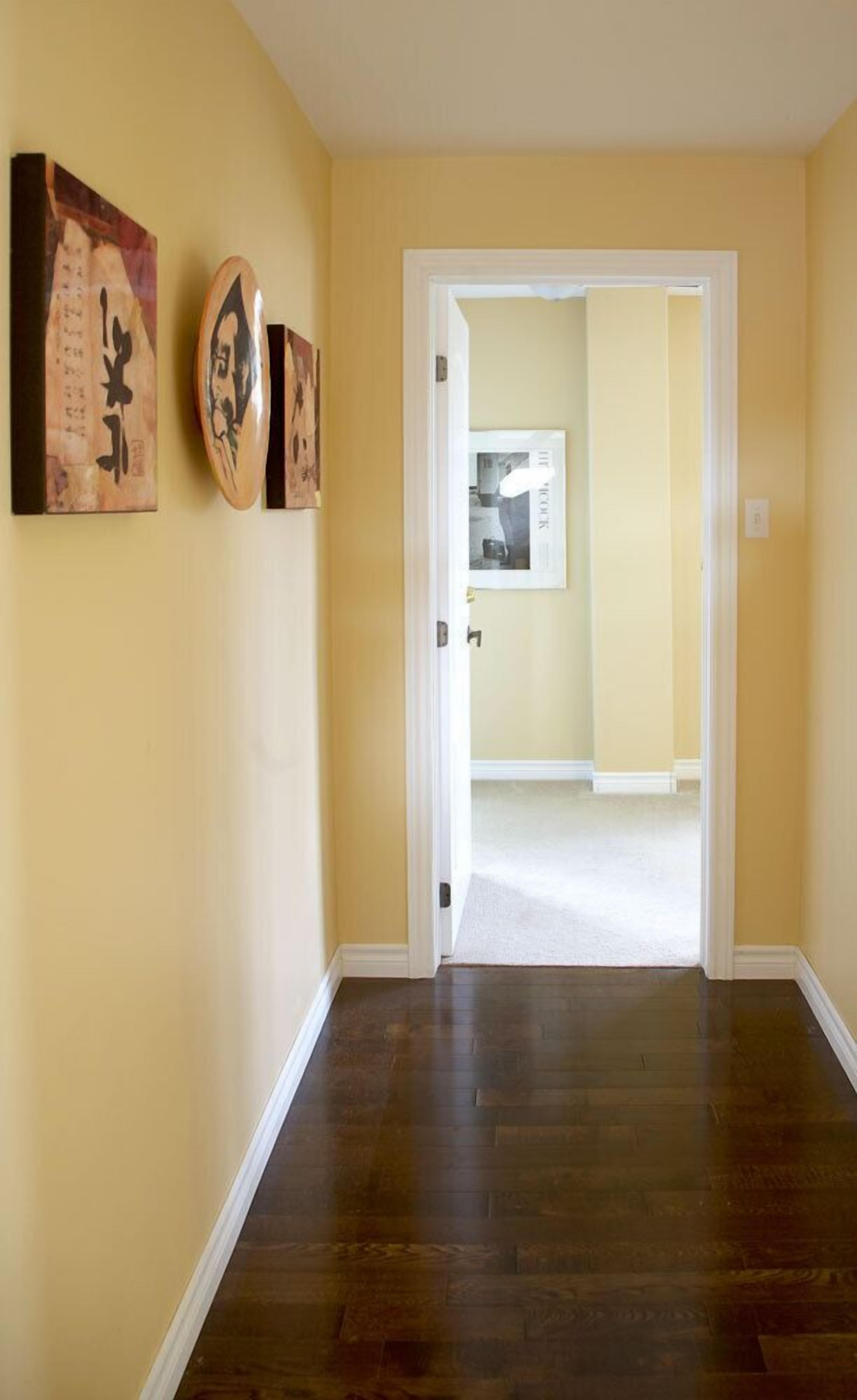 A hallway with a wooden floor, a white door, and two framed artworks on the wall.