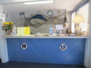 Un comptoir d’accueil décoré sur le thème de la marine, avec des éléments tels qu’un poisson, des étoiles de mer et une ancre. On y trouve des brochures d’information, un téléphone et une lampe.