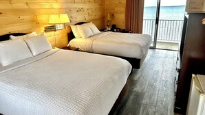 Hotellihuone, jossa on kaksi sänkyä, puupaneeliseinät, parveke, jolta on näkymä merelle, ja jääkaappi.