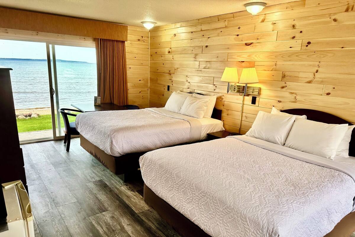 Ein Hotelzimmer mit zwei Betten, einer Holzwand, Meerblick und einem Tisch mit Stühlen.