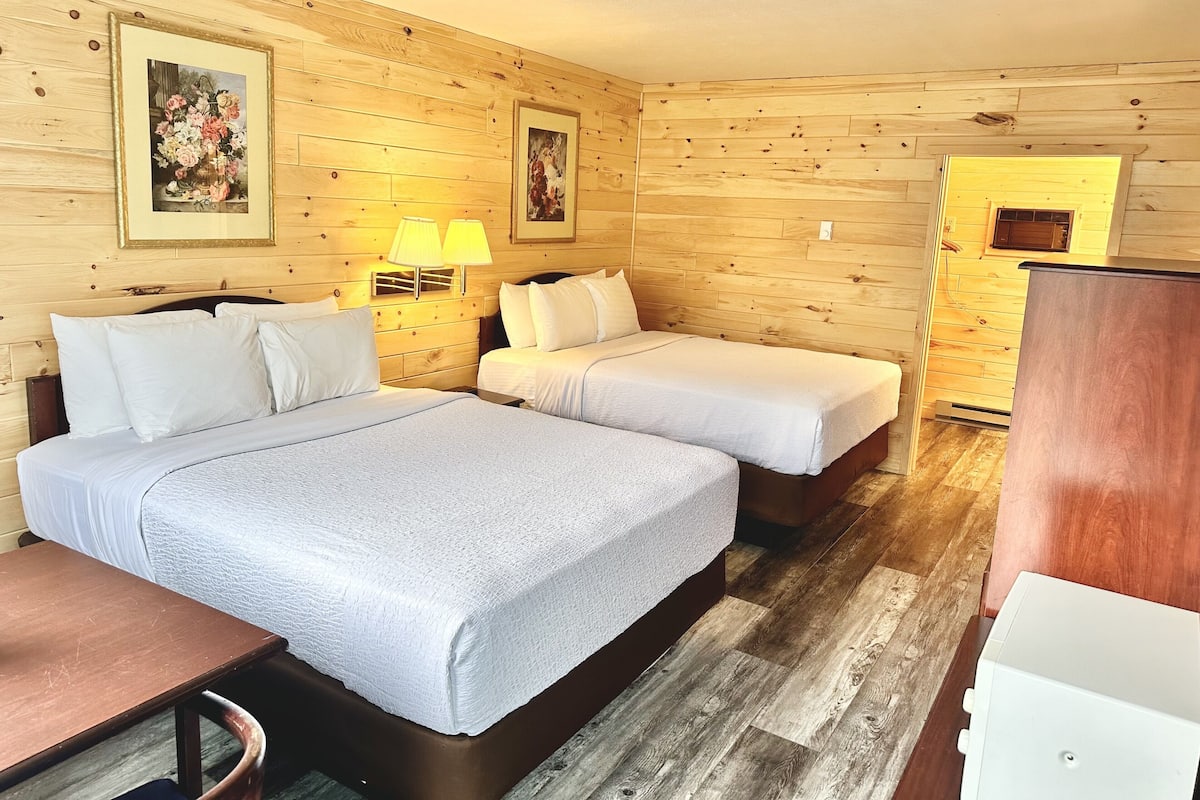 Ein Zimmer mit zwei Betten, einer Holzwand, einem Schreibtisch und einem Schrank.