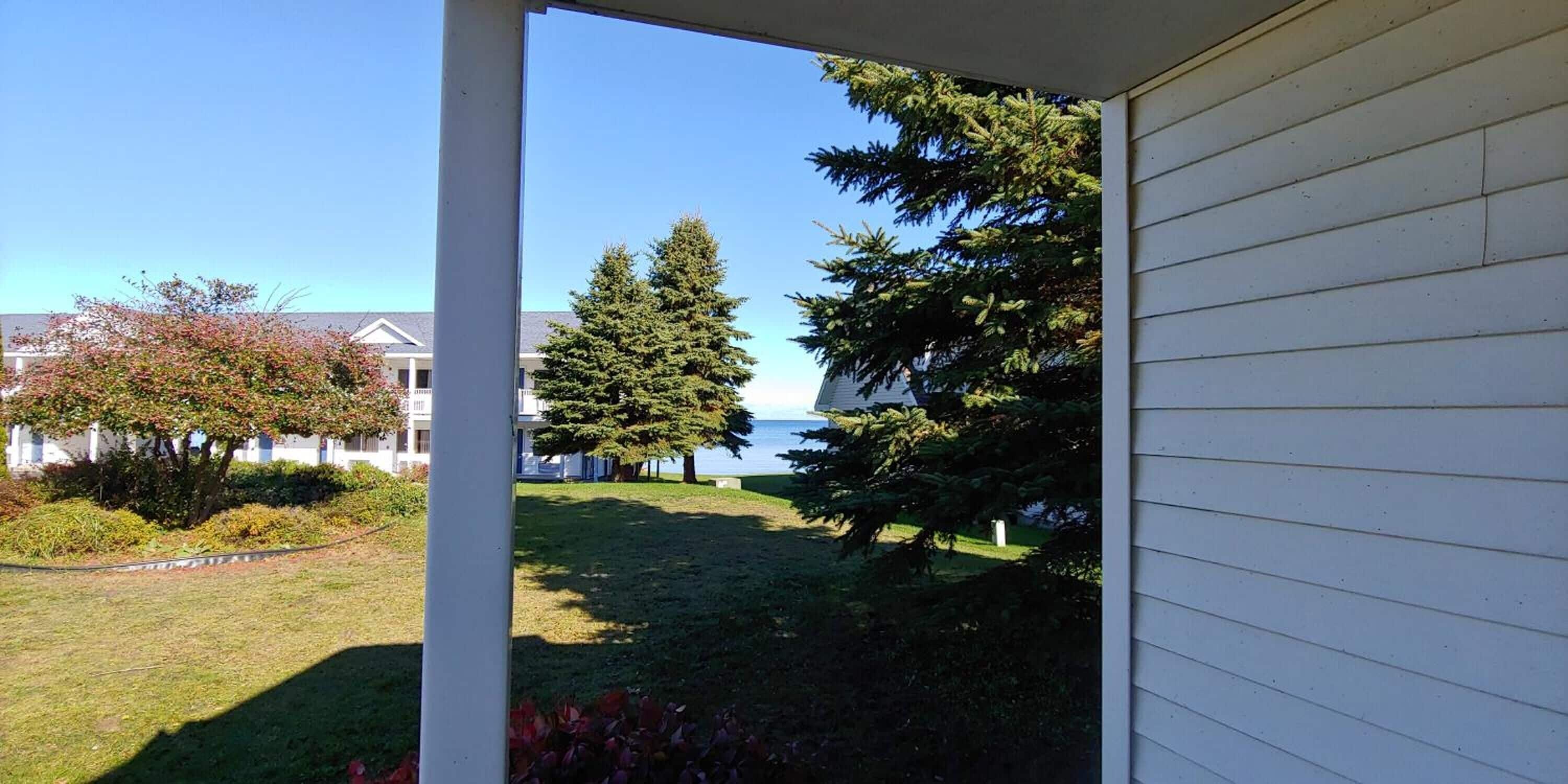 A view from a porch to a grassy area with trees and a body of water in the background.