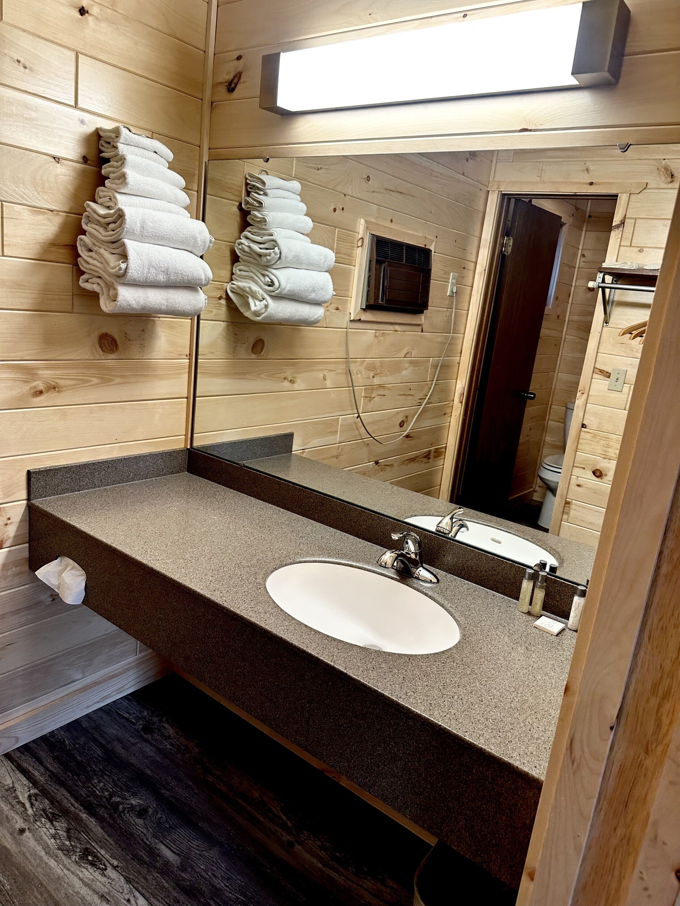 Un baño de estilo cabaña de madera con lavamanos de granito, un espejo grande y toallas ordenadas en un toallero de pared.