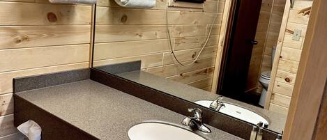 Un baño de estilo cabaña de madera con lavamanos de granito, un espejo grande y toallas ordenadas en un toallero de pared.