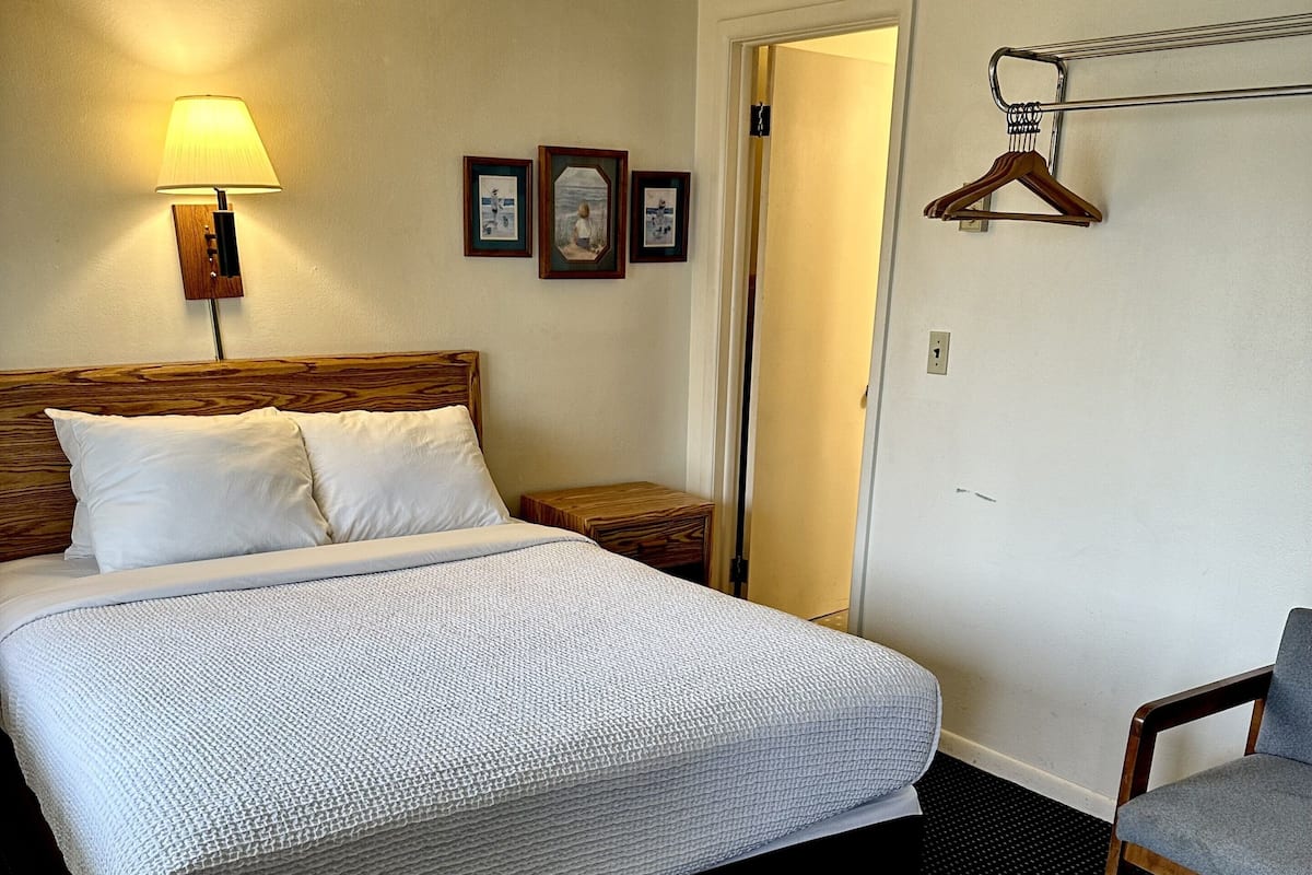 Ein Hotelzimmer mit einem Bett, einem Sessel, einem kleinen Tisch, einer Lampe und einer Tür.