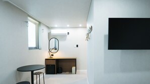 Une pièce de taille modeste, comprenant une table ronde, deux tabourets, un miroir, un petit meuble et un téléviseur fixé au mur.