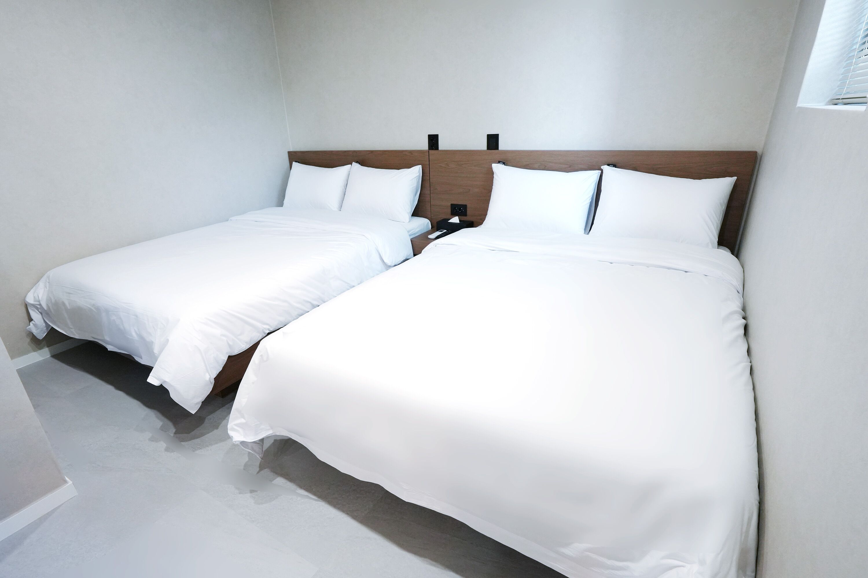 A hotel room with two single beds, a wooden headboard, and a small bedside table with a lamp.