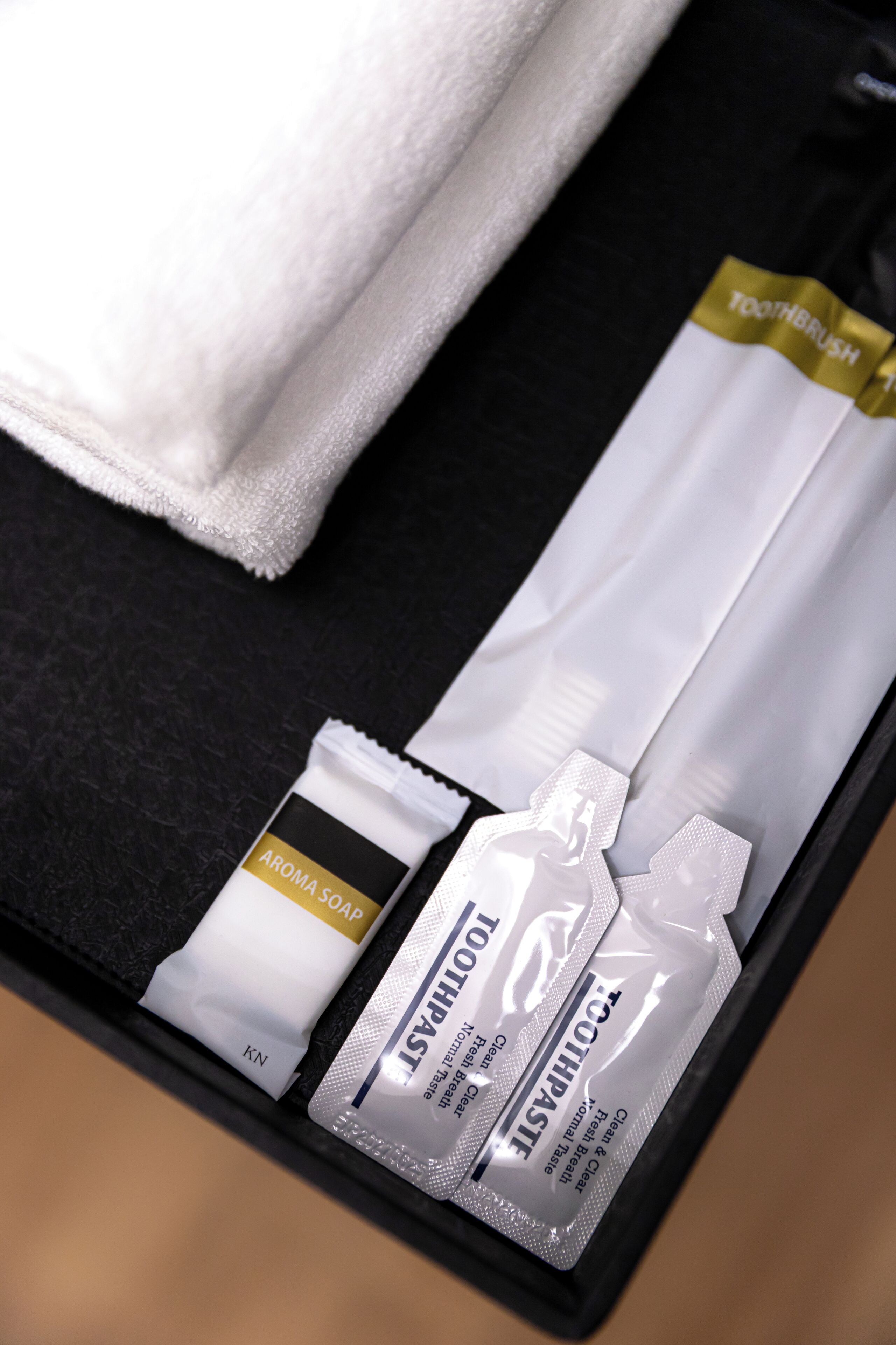 A black tray with a white towel, a toothbrush, a tube of soap, and a tube of toothpaste.