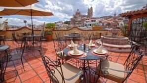 Un patio al aire libre con mesas y sillas redondas, una fuente y vistas a edificios históricos al fondo.