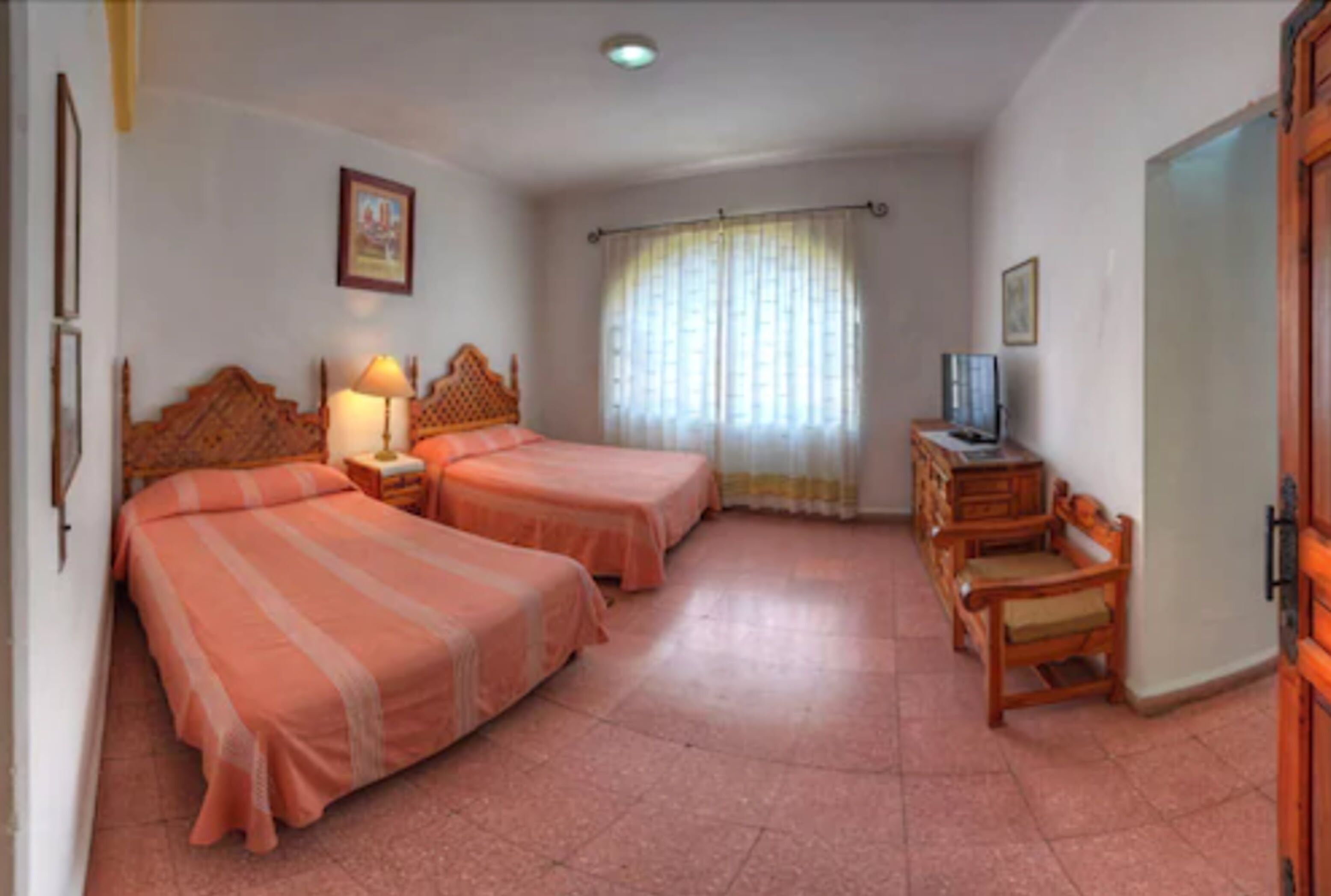 Una habitación con dos camas, televisión, un armario de madera y una ventana con cortinas.
