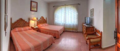 Una habitación con dos camas, televisión, un armario de madera y una ventana con cortinas.