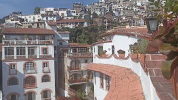 Un barrio residencial en una ladera, con tejados de tejas de terracota y paredes blancas, que presenta balcones y plantas con flores rojas.