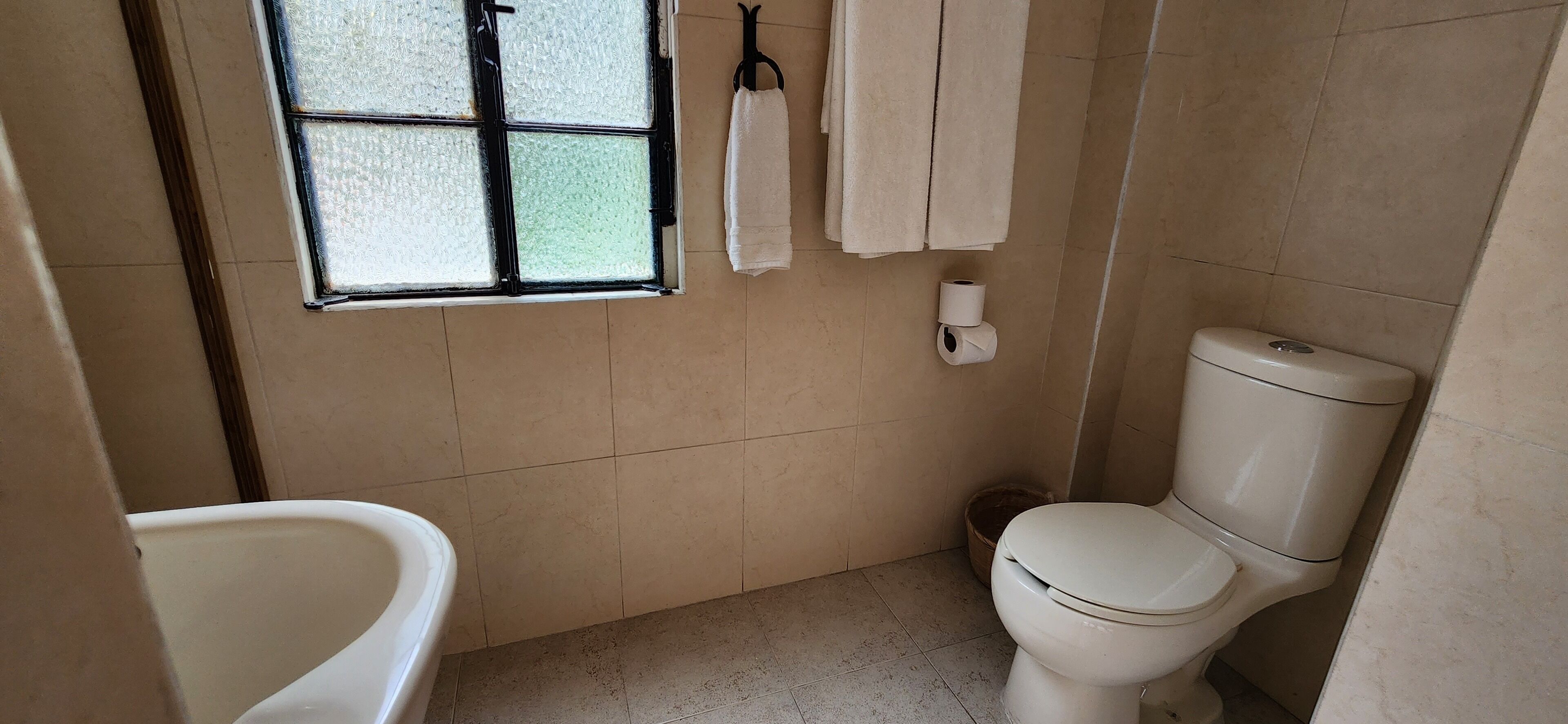 Casa de banho com sanita, uma pequena janela, porta-toalhas e suporte para papel higiénico.