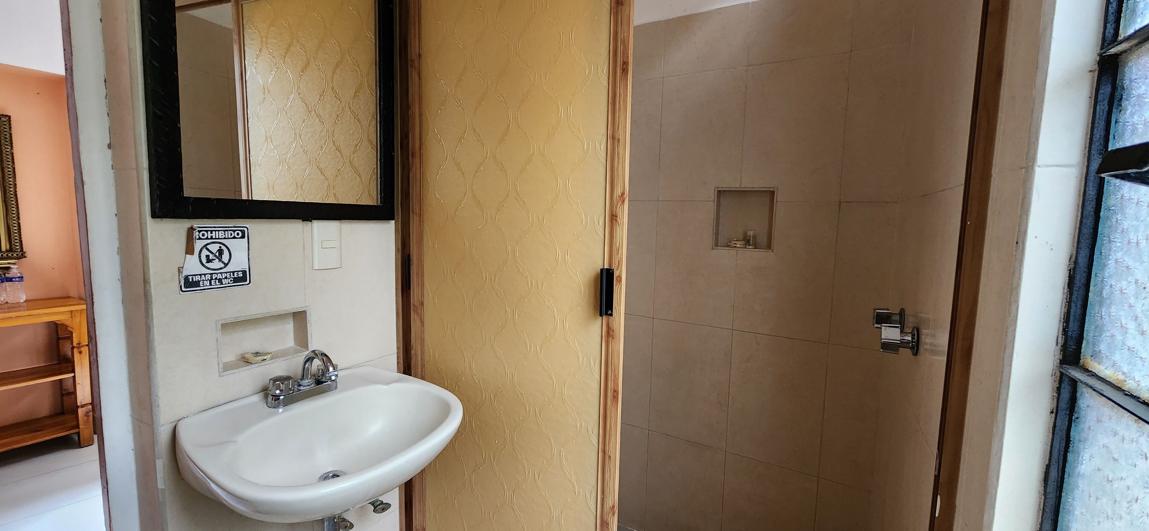 Un baño con un lavamanos blanco, un espejo y una puerta que da a la zona de la ducha.