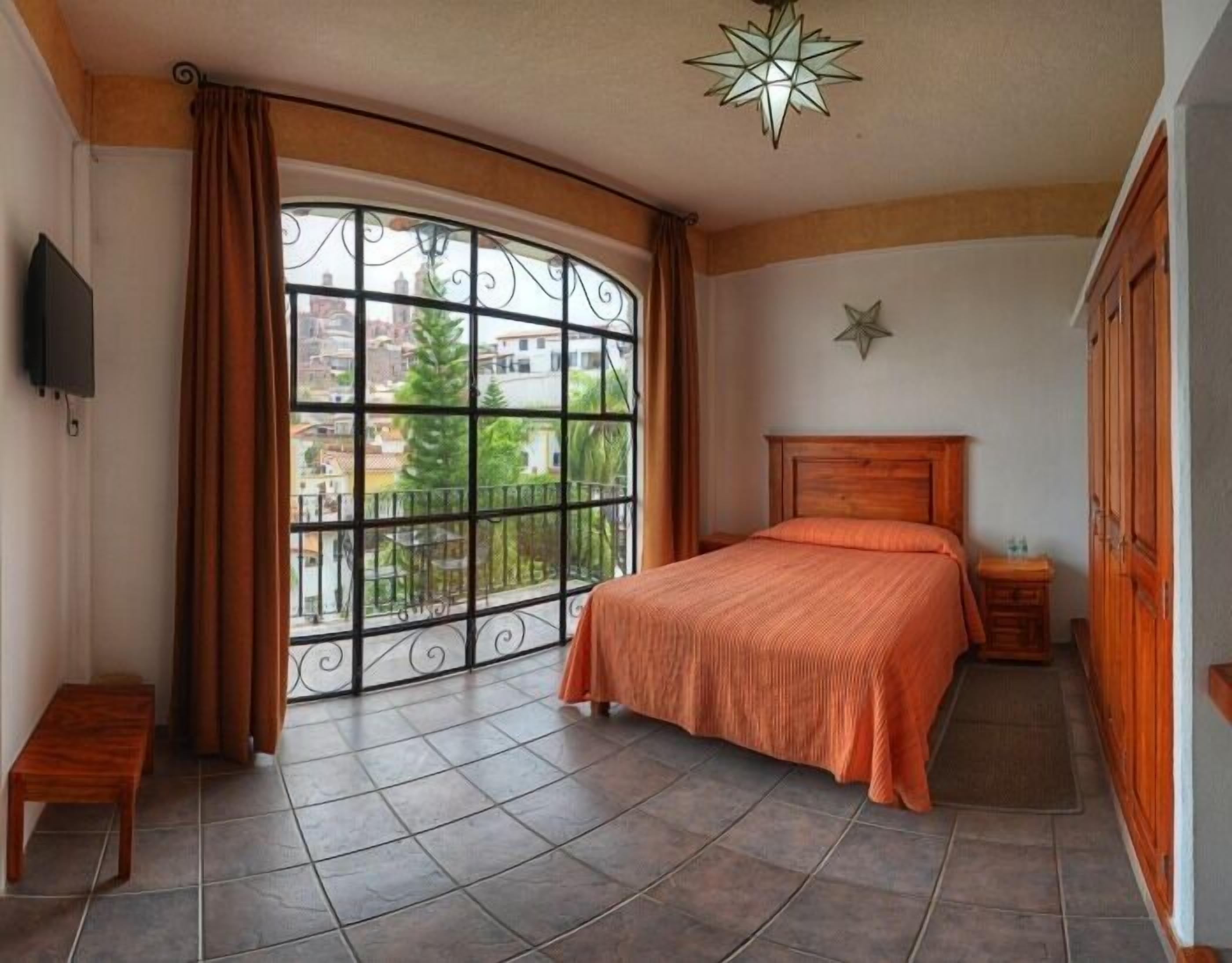 A bedroom with a large window, a bed, a nightstand, a wooden headboard, a star-shaped light fixture, and a wardrobe.