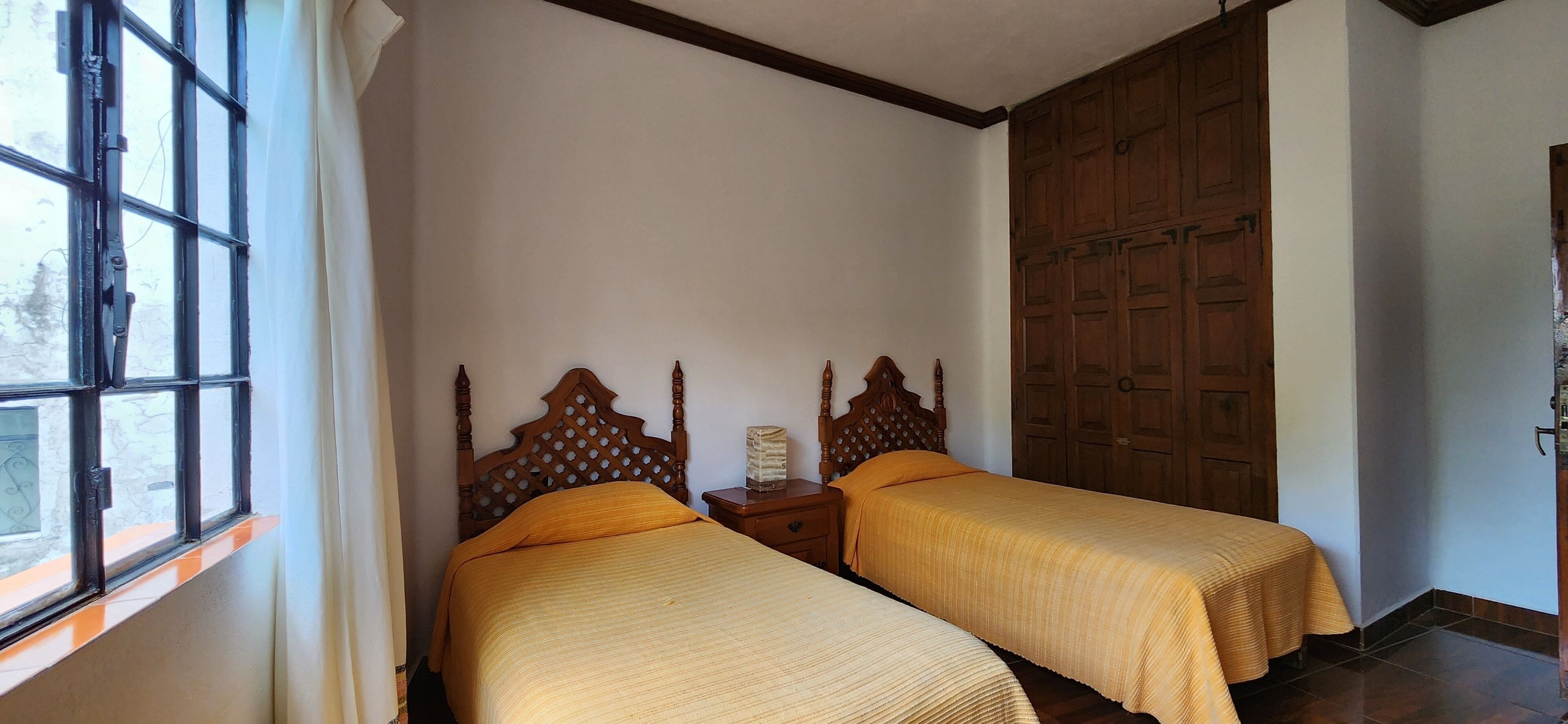 A room with two wooden beds with matching headboards, a wooden wardrobe, and a window with curtains.