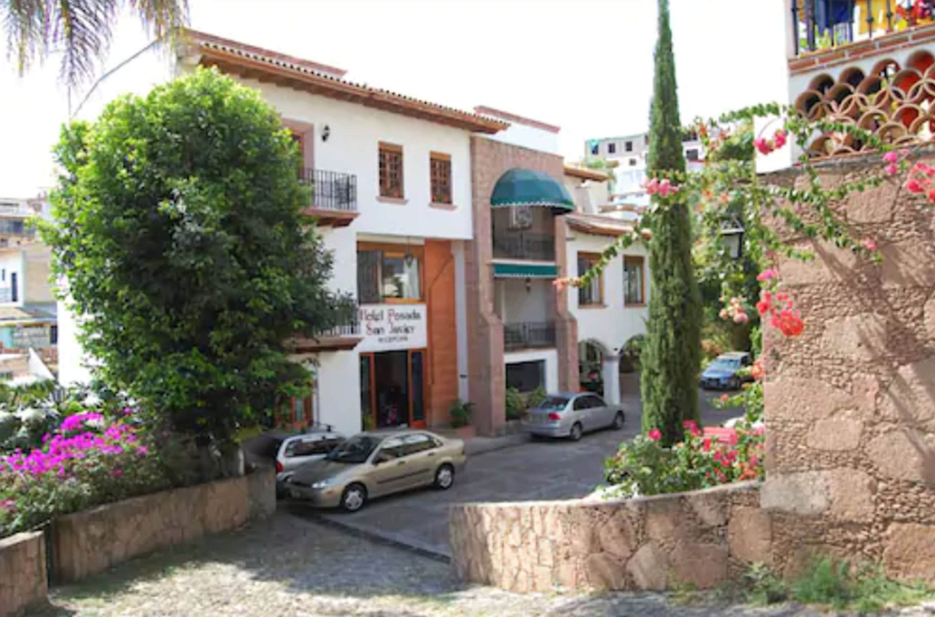 Un hotel con un letrero que dice "Hotel Posada San Jose". Tiene un camino pavimentado, coches estacionados y abundante vegetación.