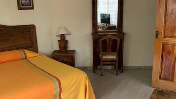 Un dormitorio con una cama, una mesita de noche de madera, una silla, un escritorio con espejo y una puerta.