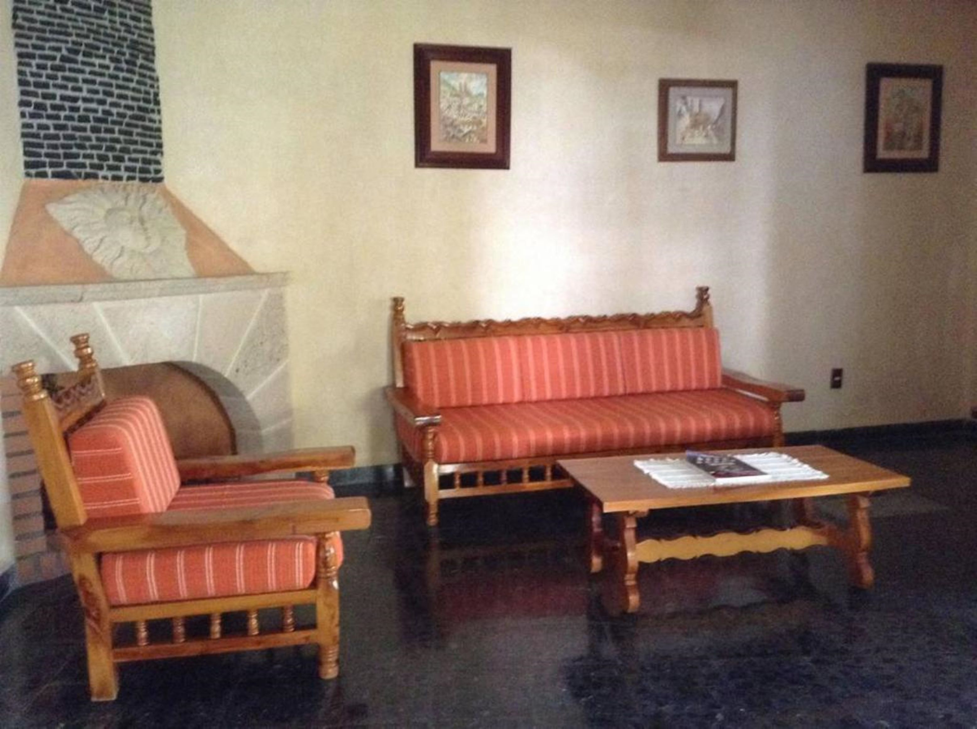 A room with a brick fireplace, a wooden sofa, a wooden armchair, and a coffee table.