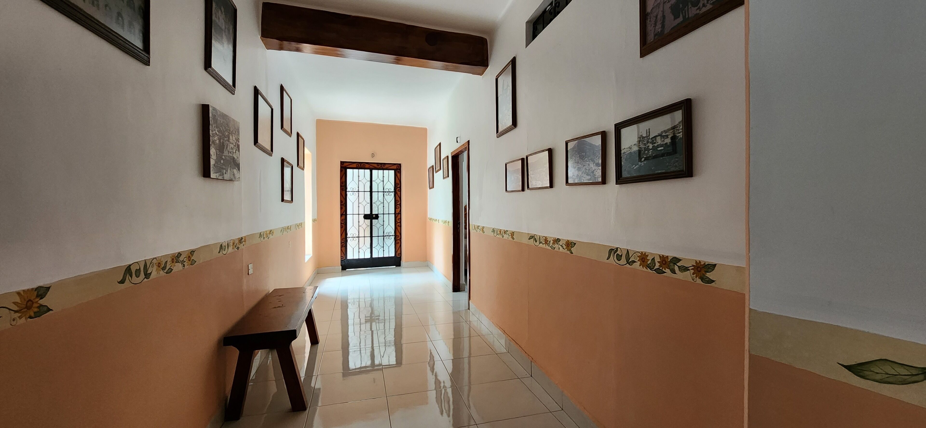 A hallway with a bench, framed pictures on the walls, and a door with a decorative gate.