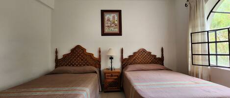Una habitación con dos camas de madera, una mesita de noche con lámpara, un cuadro en la pared y una ventana con cortinas.