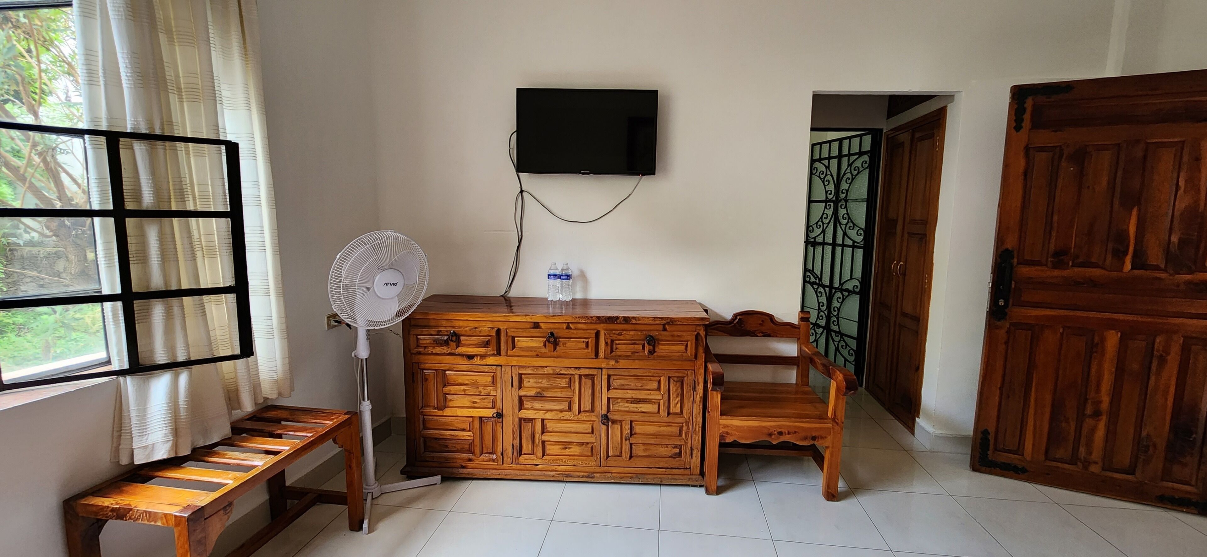 Una stanza con un armadio in legno, una TV a muro, una ventola e una panca.
