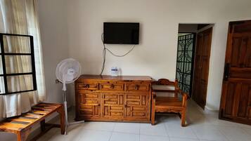 Una stanza con un armadio in legno, una TV a muro, una ventola e una panca.