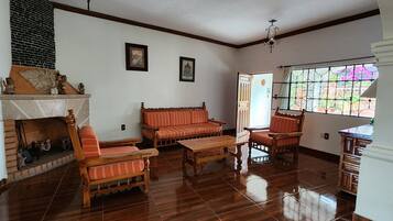 Un salon doté d’une cheminée, de meubles en bois et offrant une vue par une fenêtre ornée de barreaux décoratifs.
