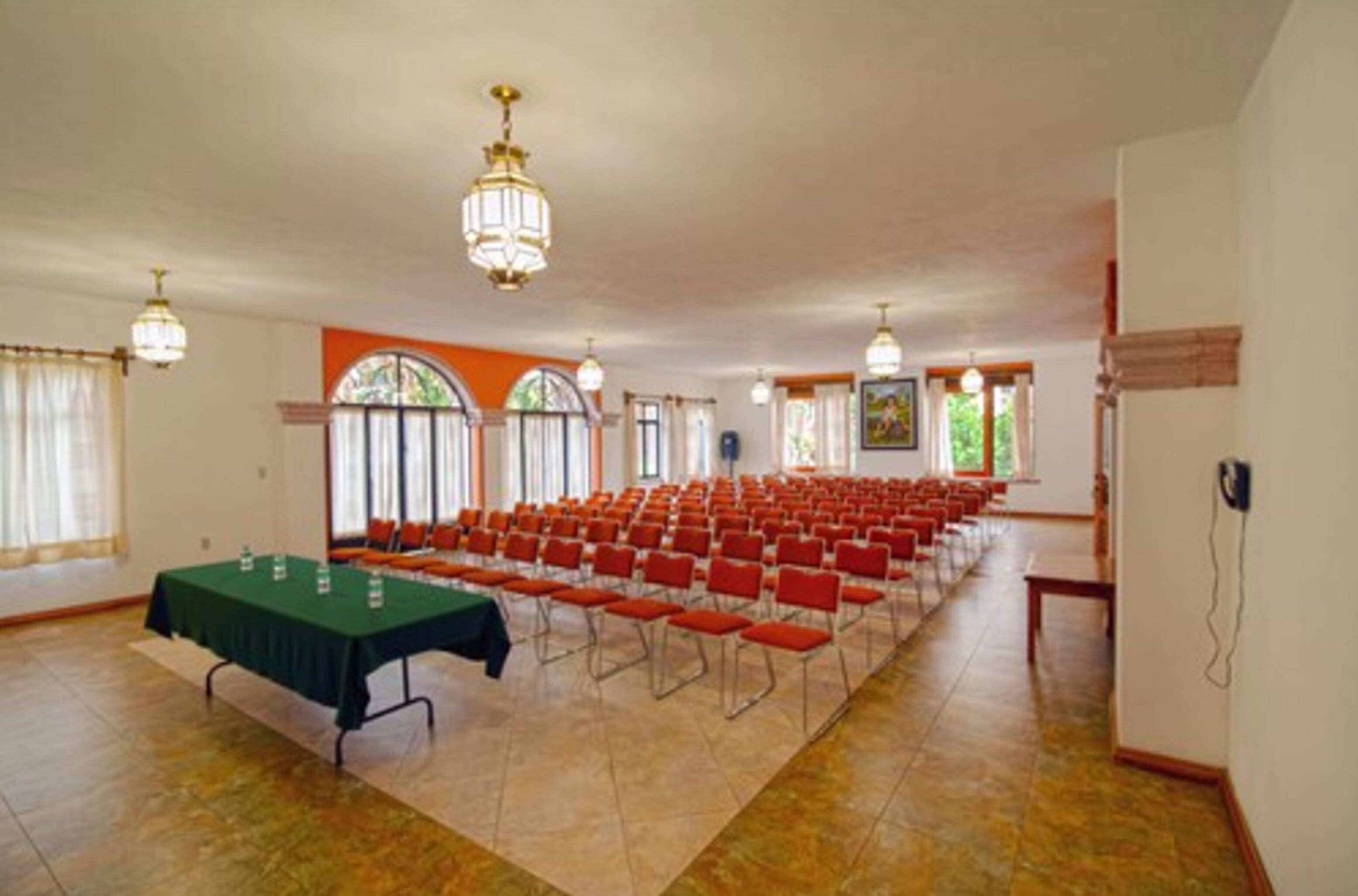 Une salle de conférence avec des rangées de chaises rouges, une table verte et un lustre.