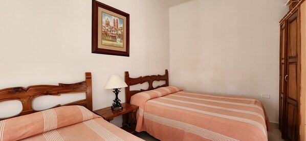 Habitación de hotel con dos camas, cabecero de madera, mesita de noche con lámpara y un cuadro en la pared.