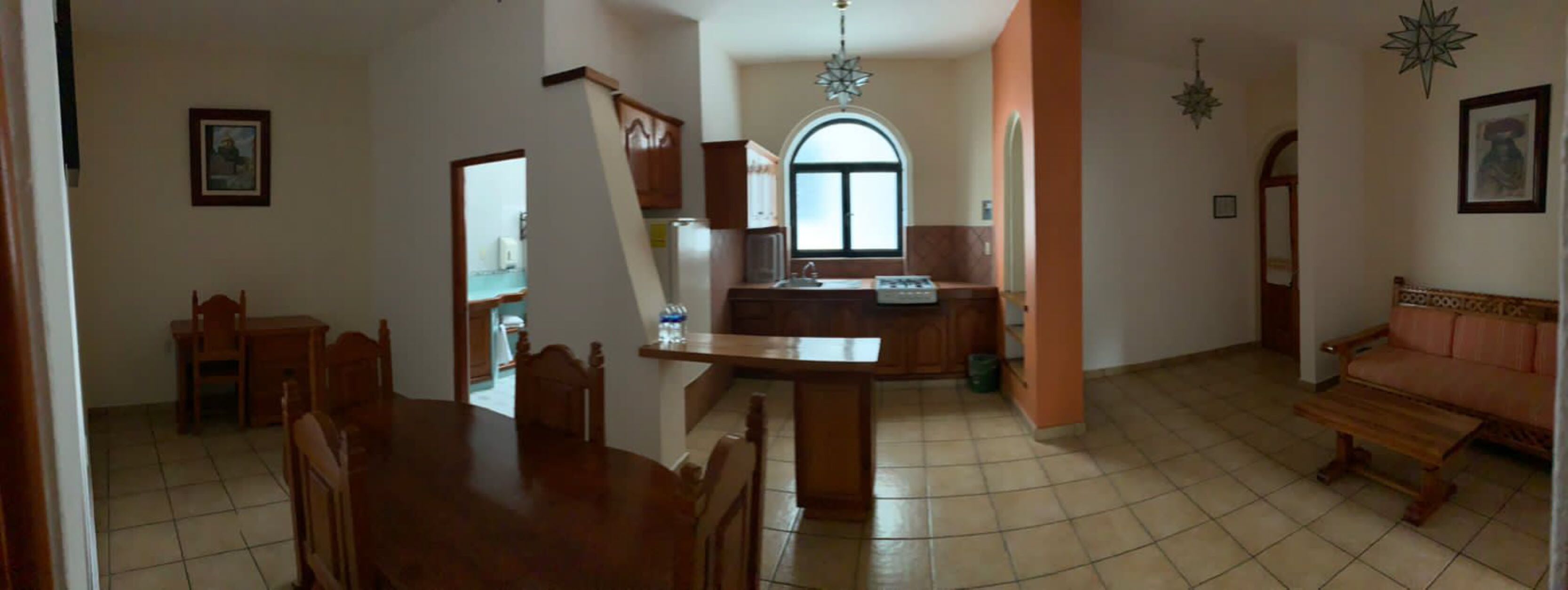 A spacious living area with a dining table and chairs, a kitchen with an arched window, and a sofa.