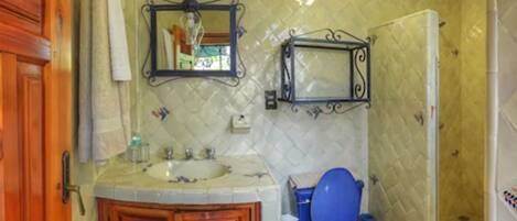 Casa de banho com toucador de madeira, lavatório, espelho, sanita e zona de duche.